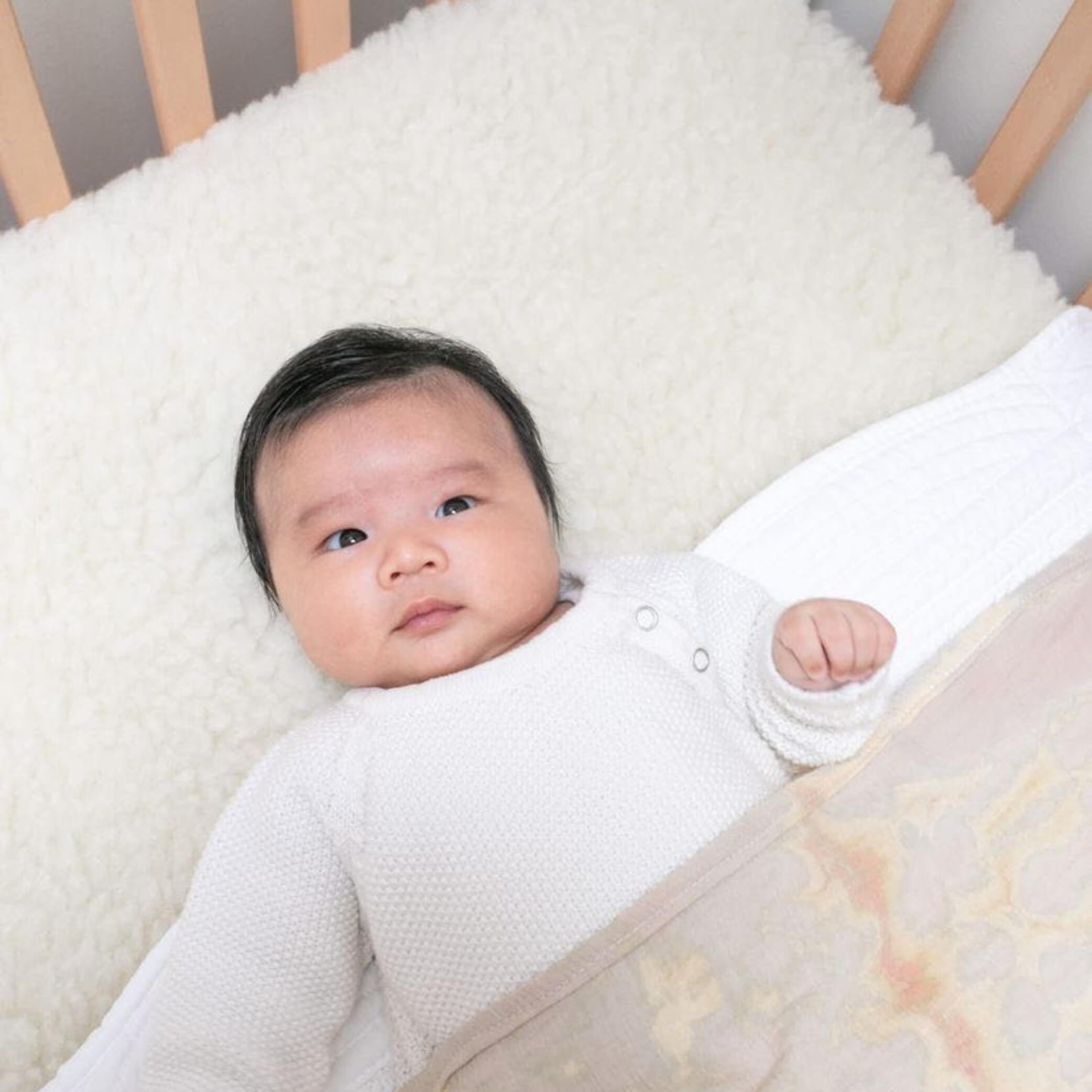 Cute baby on waterproof mattress cot topper made from Australian lambswool.
