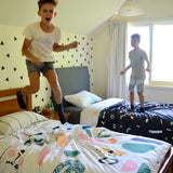 Two boys jumping excitedly on their beds.  The quilt covers are bright and colourful.