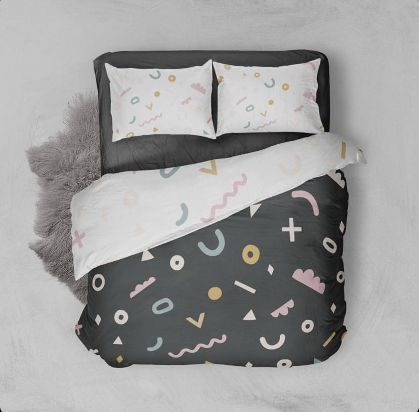 Bird's eye view of our abstract printed kids quilt cover with a black background and colourful shapes on one side and a white background and colourful shapes on the underside and pillow cases.