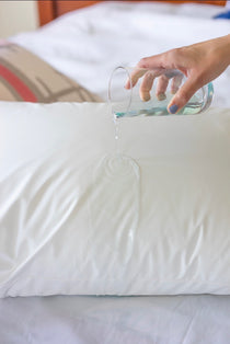 A cup of water is being poured over a white waterproof pillow.