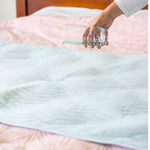 Boss 40 bed pad, on top of a bed with a lady's hand pouring liquid on it to demonstrate its waterproof and absorbent qualities