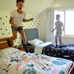 Two boys jumping excitedly on their beds.  The quilt covers are bright and colourful.