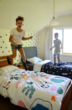 Two boys jumping excitedly on their beds.  The quilt covers are bright and colourful.
