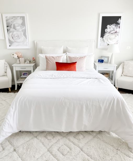 White quilt on a bed with complimenting display pillows.  There are two bedside tabels on either side and two floral print on the wall above.