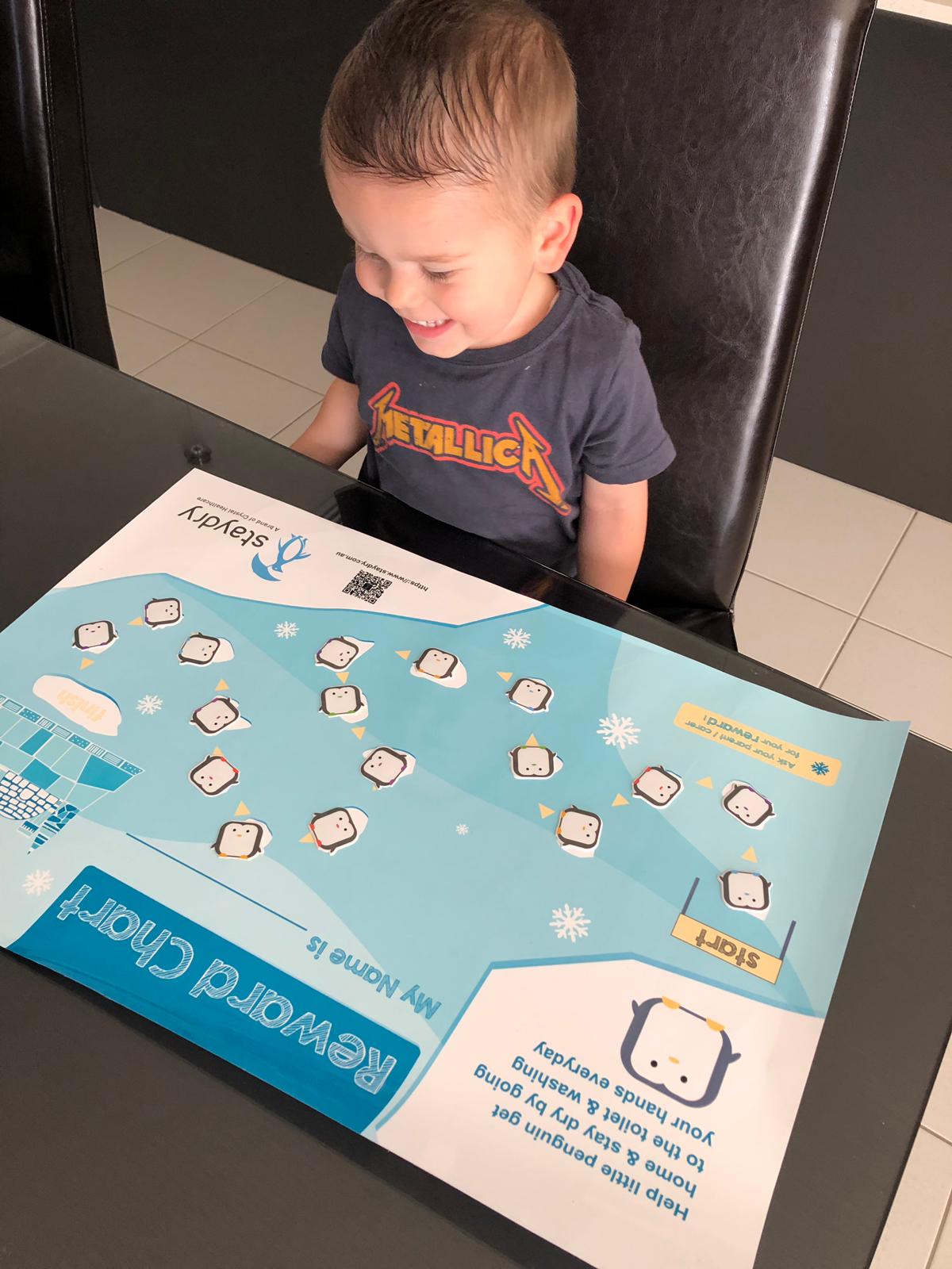 Little boy smiling at his toilet training chart.
