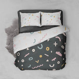 Bird's eye view of our abstract printed kids quilt cover with a black background and colourful shapes on one side and a white background and colourful shapes on the underside and pillow cases.