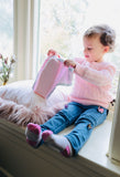 Toddler girl in a pink jumper sitting by a light filled window holding a pair of pink incontinence briefs