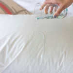 A cup of water is being poured over a white waterproof pillow.