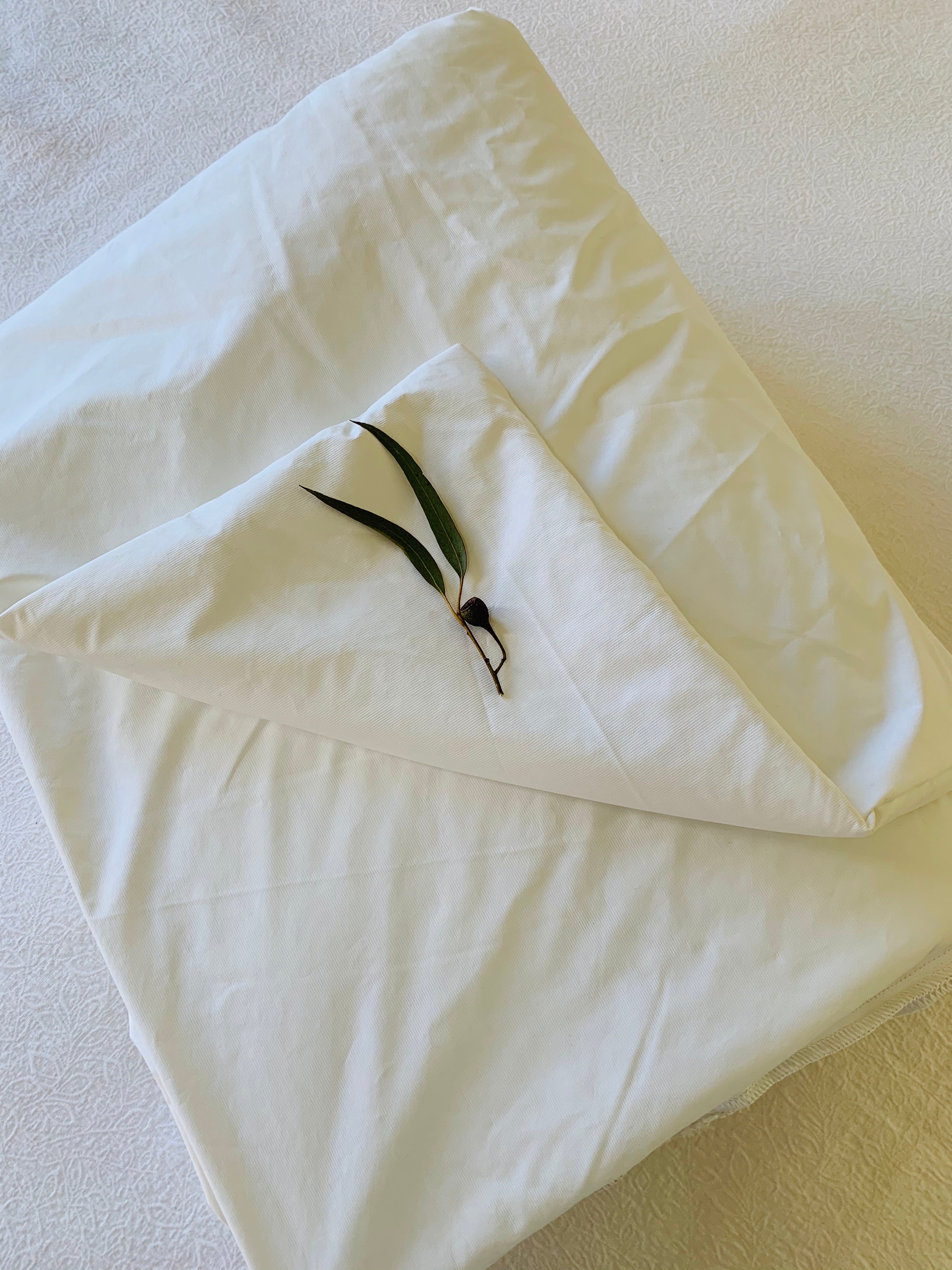 A white quilt that has been folded and has Australian gumtrees leaves and nuts resting on top.