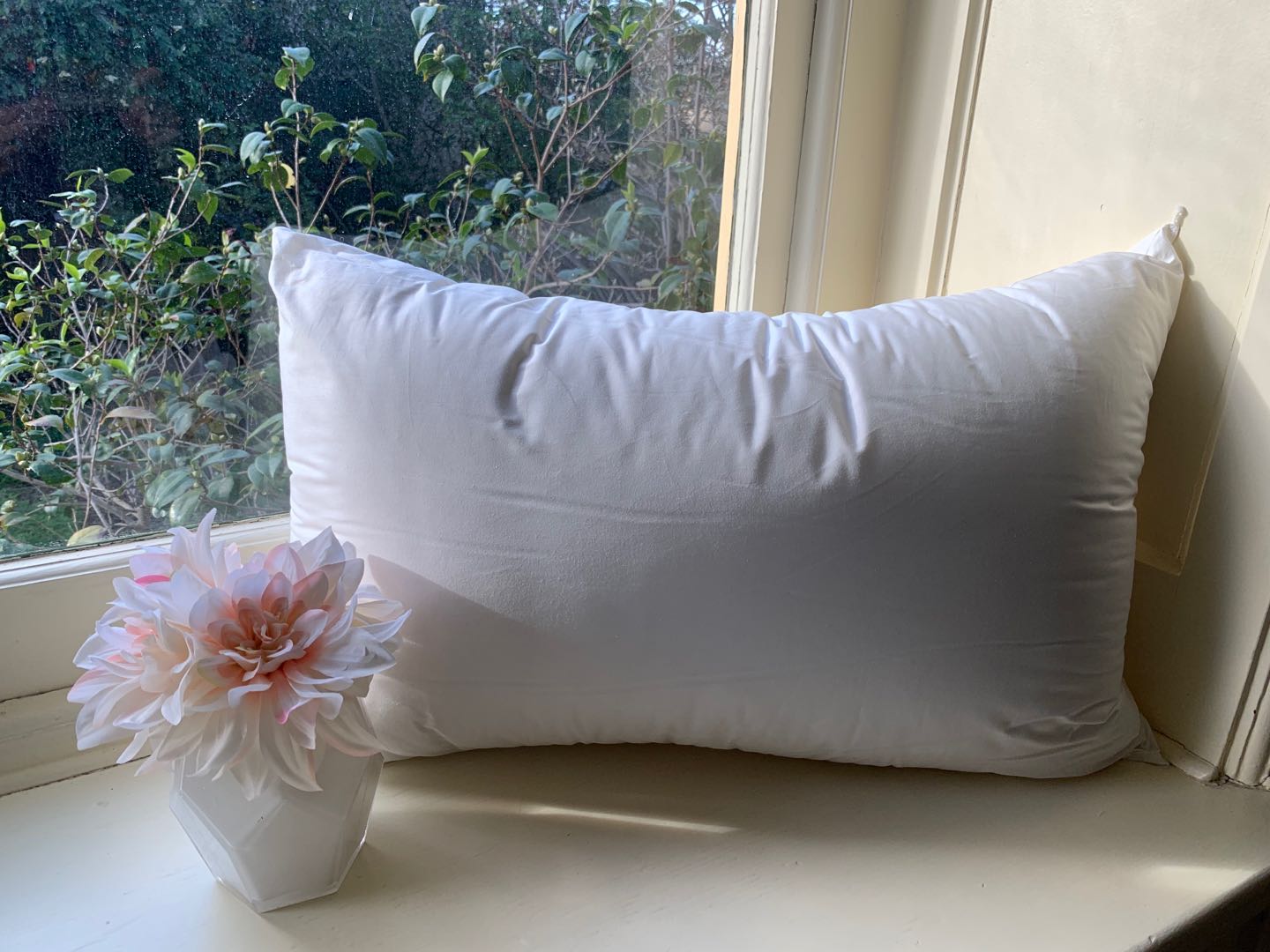 Pillow sitting against a windowsill with pink flowers nearby.